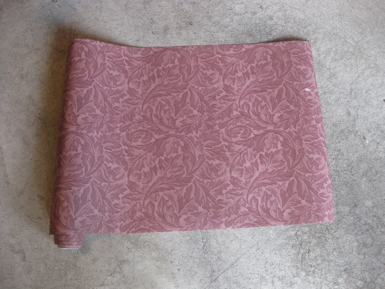 A partially unrolled mauve wallpaper with a repeating leaf pattern.